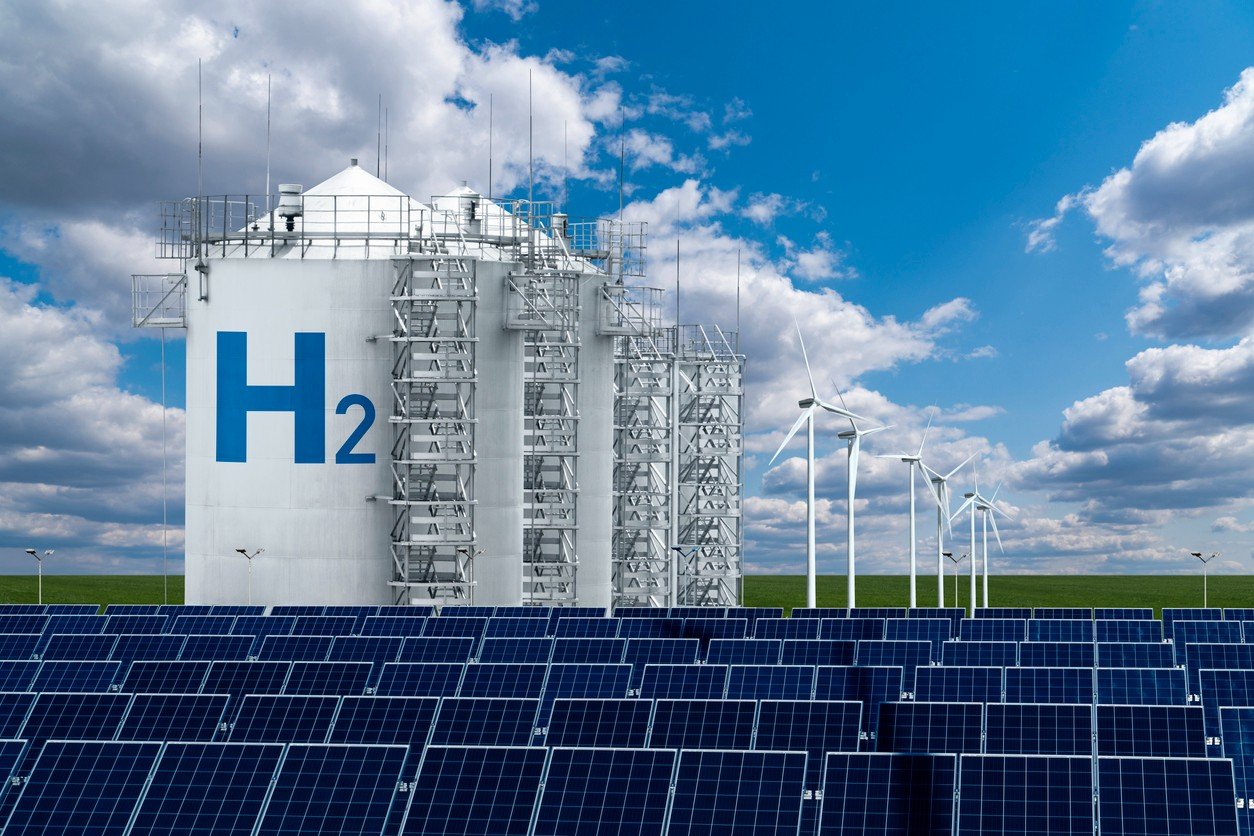Hydrogen plant silos against a blue sky with clouds and solar panels in the foreground.